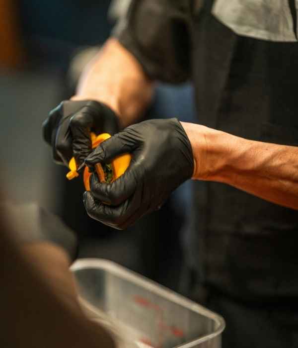 Gloved hands peeling produce over a stainless-steel hotel pan