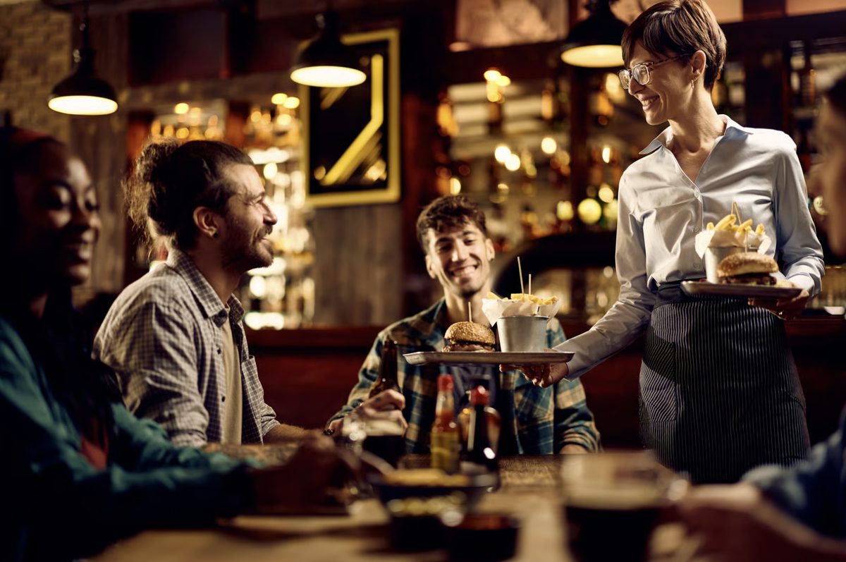 A server delivering plates to a table of guests in a busy restaurant