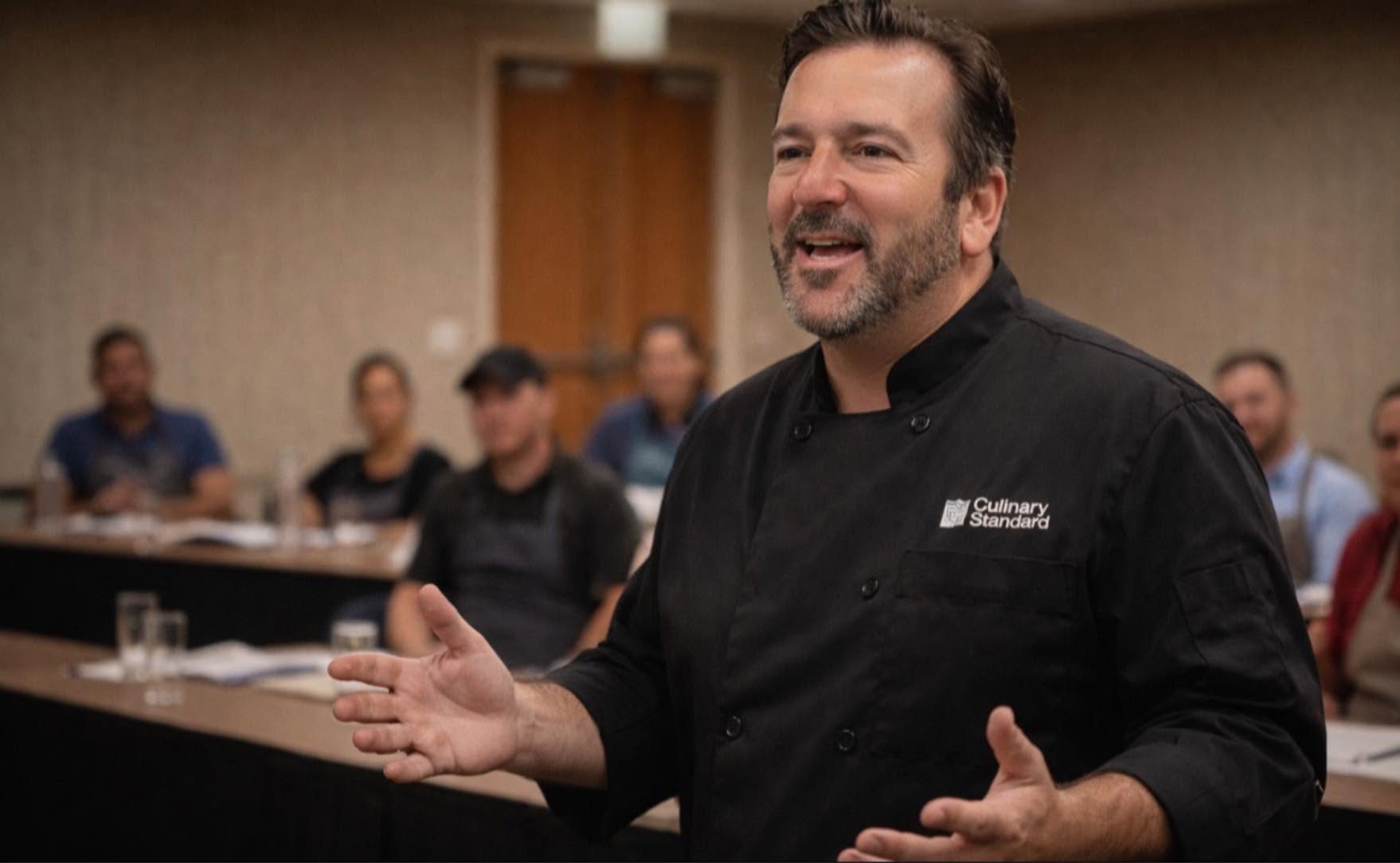 Jim Murray, founder of Culinary Standard, teaching a class in a black Culinary Standard chef coat