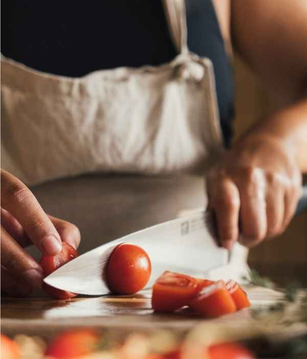 Hands slicing tomatoes on a cutting board with a chef knife